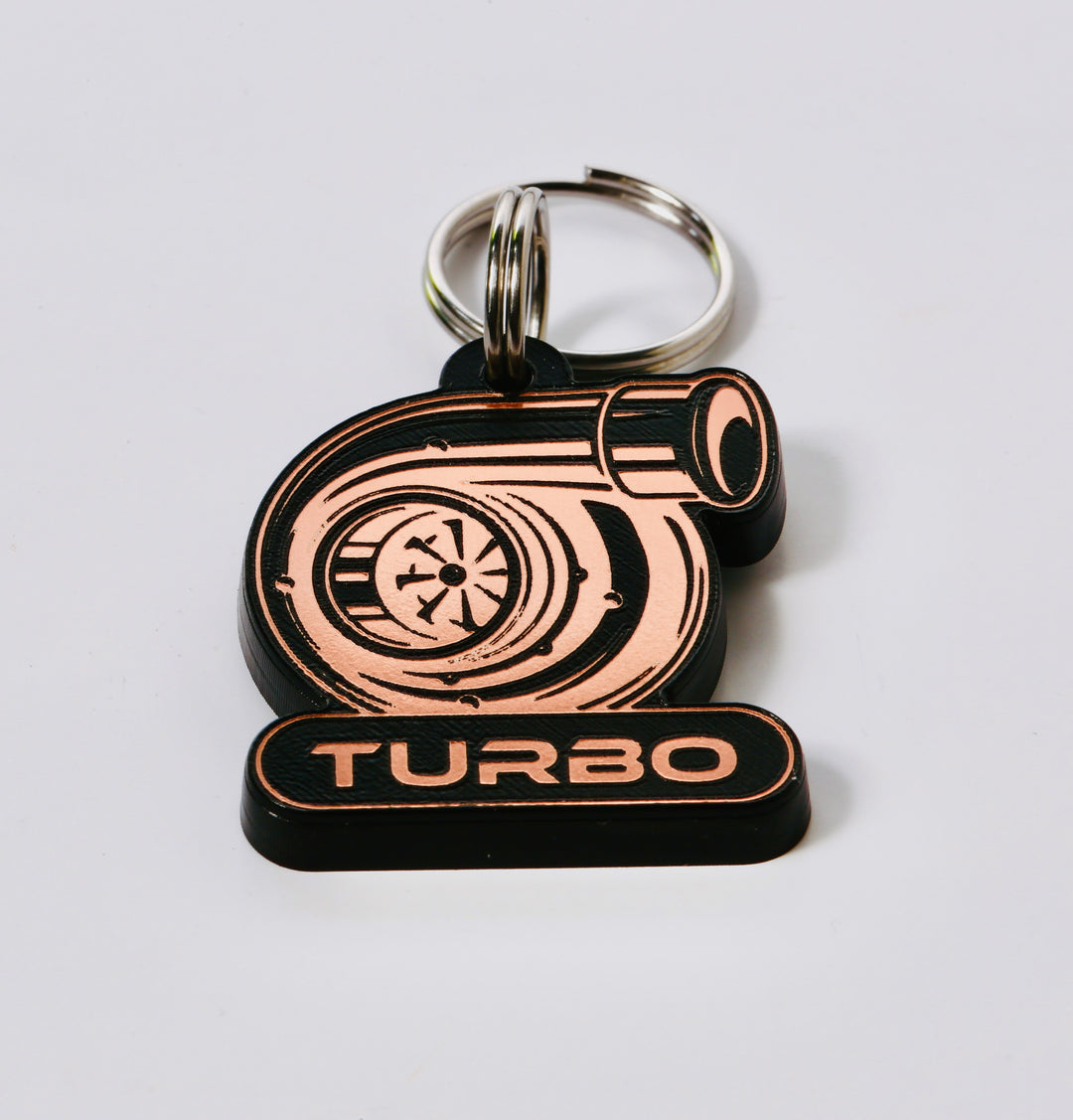 A keychain with a metallic design featuring a large engine or turbocharger and the word "TURBO" written on it.